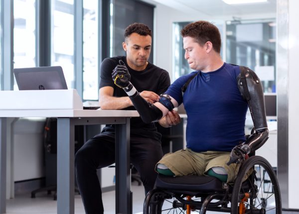 Homme aidant une personne avec des bras prothétiques dans un fauteuil roulant
