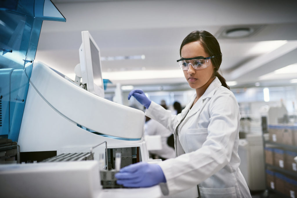 Femme portant une blouse de laboratoire et des lunettes protectrices devant une machine