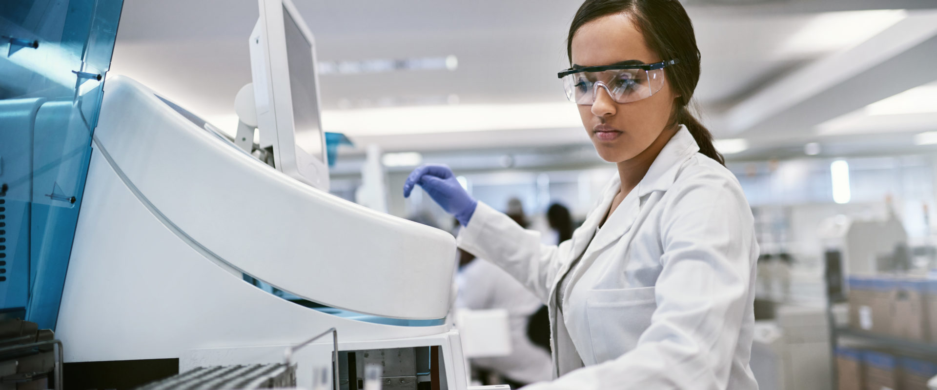 Femme portant une blouse de laboratoire et des lunettes protectrices devant une machine